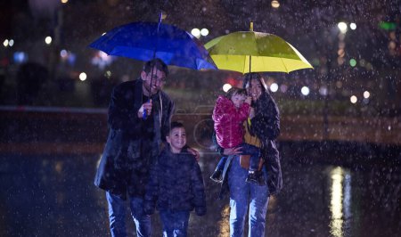 Mitten in einer regnerischen Stadtnacht spaziert ein glückliches Paar mit seinen Kindern durch die Straßen der Stadt in Richtung Kino für einen entzückenden Familienausflug..