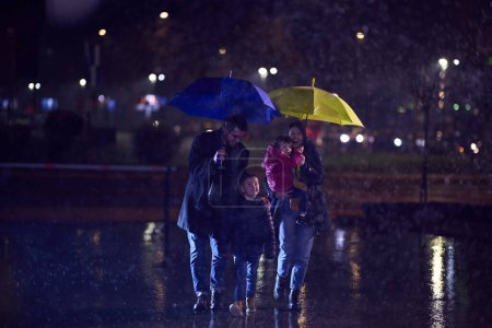 In the midst of a rainy urban night, a happy couple takes their children on a stroll through the city streets, heading towards the cinema for a delightful family movie outing.