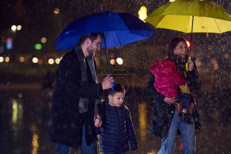 In the midst of a rainy urban night, a happy couple takes their children on a stroll through the city streets, heading towards the cinema for a delightful family movie outing.
