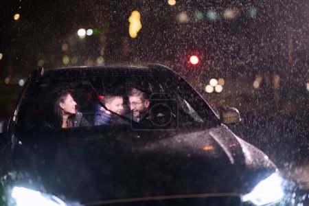In the midst of a nighttime journey, a happy family enjoys playful moments inside a car as they travel through rainy weather, illuminated by the glow of headlights, laughter, and bonding.
