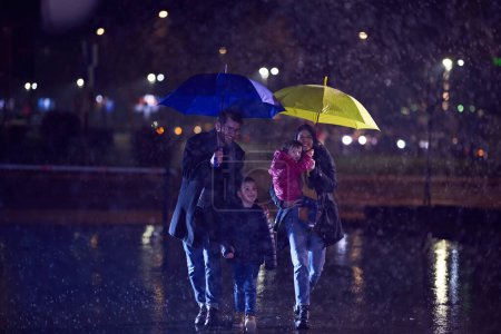 Mitten in einer regnerischen Stadtnacht spaziert ein glückliches Paar mit seinen Kindern durch die Straßen der Stadt in Richtung Kino für einen entzückenden Familienausflug..