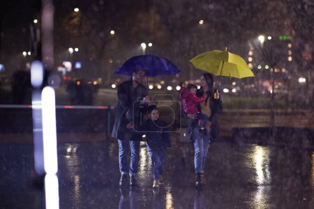 Photo for In the midst of a rainy urban night, a happy couple takes their children on a stroll through the city streets, heading towards the cinema for a delightful family movie outing. - Royalty Free Image