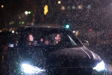 Téléchargez les photos : Au milieu d'un voyage nocturne, une famille heureuse profite de moments ludiques à l'intérieur d'une voiture alors qu'ils voyagent par temps pluvieux, illuminés par la lueur des phares, des rires et des liens. - en image libre de droit