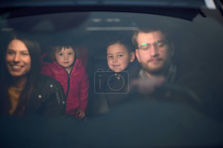 In den Nachtstunden genießt eine glückliche Familie verspielte Momente zusammen im Auto auf einer nächtlichen Roadtrip, beleuchtet vom Schein der Scheinwerfer und erfüllt von Lachen und Freude..