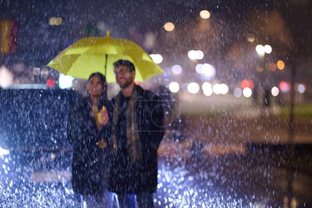 In the romantic ambiance of a rainy night, a happy couple walks through the city, sharing tender moments under a yellow umbrella, surrounded by the glistening glow of urban lights.