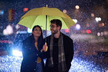 In the romantic ambiance of a rainy night, a happy couple walks through the city, sharing tender moments under a yellow umbrella, surrounded by the glistening glow of urban lights.