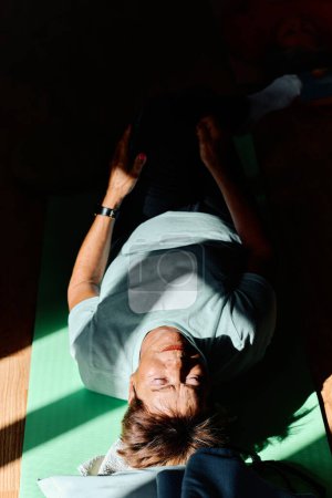 Foto de En un espacio iluminado por el sol, una mujer mayor practica con gracia el yoga rejuvenecedor, centrándose en los estiramientos del cuello, la espalda y las piernas, encarnando la serenidad y el bienestar.. - Imagen libre de derechos