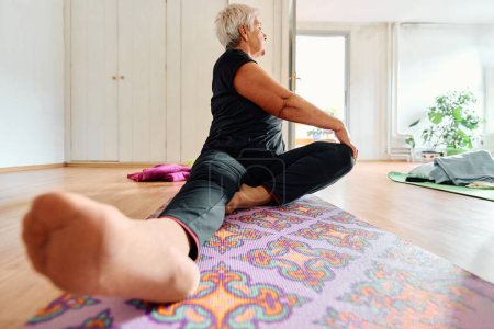 Foto de Una anciana se involucra graciosamente en varias poses de yoga, estirando sus extremidades y encontrando serenidad en un espacio moderno iluminado por el sol bajo la guía de un instructor entrenado, encarnando la esencia de - Imagen libre de derechos