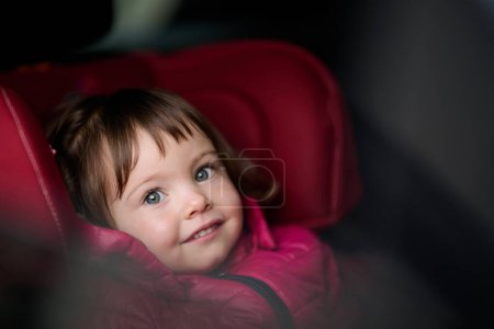 Téléchargez les photos : Une jeune fille s'assoit confortablement dans un siège d'auto moderne, sécurisée et prête pour une aventure familiale sur la route - en image libre de droit