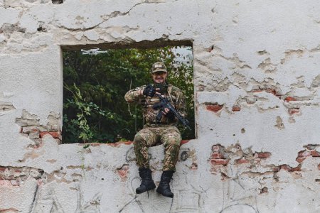 Téléchargez les photos : Un soldat est assis près de la fenêtre d'une maison récemment conquise, réfléchissant sur le triomphe et contemplant les défis rencontrés pendant la campagne militaire, capturant un moment de solitude et - en image libre de droit