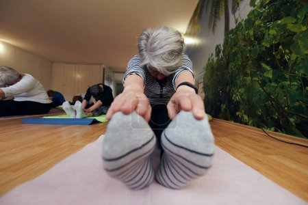 Photo for An elderly woman gracefully engages in various yoga poses, stretching her limbs and finding serenity in a modern sunlit space under the guidance of a trained instructor, embodying the essence of - Royalty Free Image