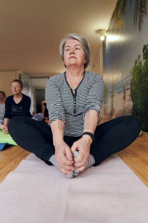 Téléchargez les photos : Une femme âgée s'engage gracieusement dans diverses poses de yoga, étirant ses membres et trouvant la sérénité dans un espace moderne ensoleillé sous la direction d'un instructeur formé, incarnant l'essence de - en image libre de droit