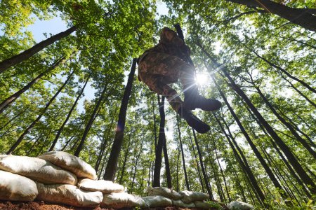 Un soldat d'élite franchit habilement les barrières militaires sur un terrain boisé périlleux, faisant preuve d'habileté tactique et d'agilité lors d'un entraînement spécialisé. 