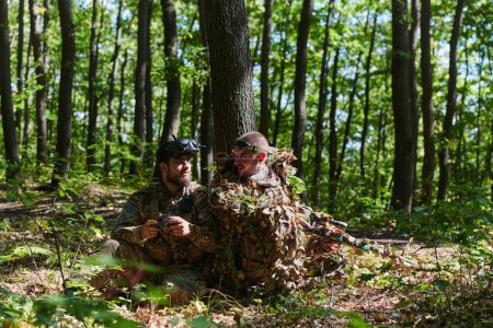 A skilled sniper and a soldier operating a drone with VR goggles strategize and observe the military action while concealed in the forest. 