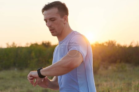 Photo for Amidst the sunny ambiance, an athlete glances at his smartwatch while running, blending technology with fitness seamlessly under the suns rays. - Royalty Free Image