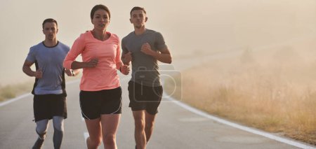 Photo for A group of friends, athletes, and joggers embrace the early morning hours as they run through the misty dawn, energized by the rising sun and surrounded by the tranquil beauty of nature. - Royalty Free Image