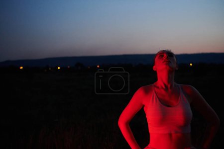 Téléchargez les photos : Après une course nocturne épuisante, un athlète prend une pose confiante, baignée dans la lueur rouge de l'environnement, montrant à la fois épuisement et détermination.. - en image libre de droit