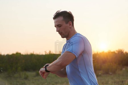 Foto de En medio del ambiente soleado, un atleta mira su reloj inteligente mientras corre, combinando la tecnología con la forma física sin problemas bajo los rayos del sol. - Imagen libre de derechos