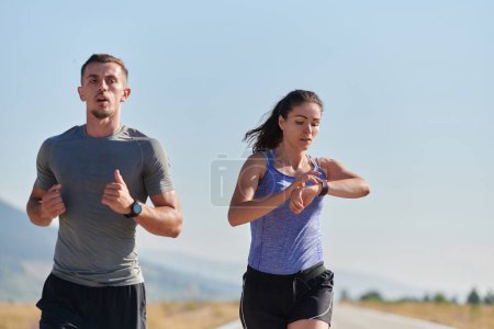 Foto de Una pareja corre a través de un camino cubierto de sol, sus cuerpos fuertes y sanos, su amor por los demás y el aire libre evidente en cada paso. - Imagen libre de derechos
