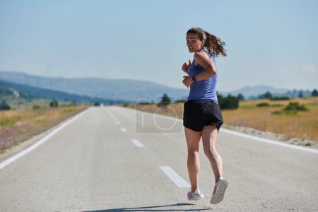 Photo for An athletic woman finds freedom and joy in a healthy lifestyle, running through a beautiful road trail at sunrise. - Royalty Free Image