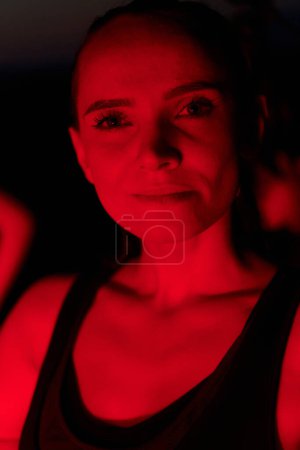 After a grueling nighttime run, an athlete strikes a confident pose, bathed in the red glow of the surroundings, showcasing both exhaustion and determination.