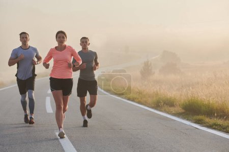 Photo for A group of friends, athletes, and joggers embrace the early morning hours as they run through the misty dawn, energized by the rising sun and surrounded by the tranquil beauty of nature. - Royalty Free Image