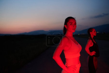 Photo for After a grueling nighttime run, an athlete strikes a confident pose, bathed in the red glow of the surroundings, showcasing both exhaustion and determination. - Royalty Free Image