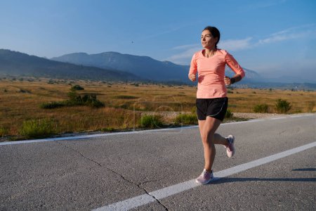 Foto de Una atleta resuelta y motivada corriendo con confianza hacia el amanecer, personificando la determinación y el empoderamiento en su carrera matutina. - Imagen libre de derechos