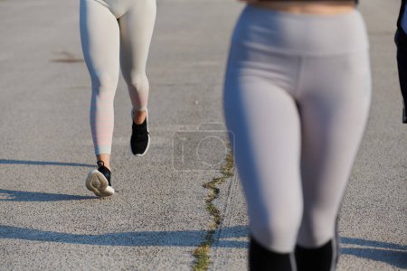 The muscular legs of an athletic runner are captured in motion, illuminated by the sunlight on a bright day.