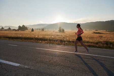 Photo for A resolute and motivated athlete running confidently into the sunrise, epitomizing determination and empowerment in her early morning run. - Royalty Free Image