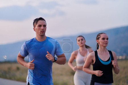Foto de Un grupo diverso de corredores encuentra motivación e inspiración en el otro mientras entrenan juntos para una próxima competencia, en un escenario de puesta de sol impresionante. - Imagen libre de derechos