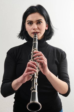 Eine talentierte brünette Musikerin zeigt ihre Kunstfertigkeit, als sie anmutig die Klarinette vor einem makellosen weißen Hintergrund hält und spielt