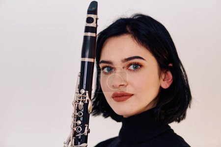 Photo for A talented brunette musician showcases her artistry as she gracefully holds and plays the clarinet against a pristine white background - Royalty Free Image