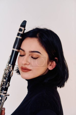 Foto de Una talentosa música morena exhibe su arte mientras sostiene con gracia y toca el clarinete sobre un fondo blanco prístino - Imagen libre de derechos