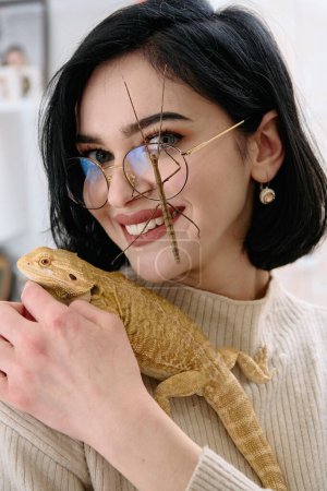 Téléchargez les photos : Une jeune femme pose avec ses deux animaux de compagnie, un dragon barbu et un insecte bâton, sur cette photo chaleureuse. - en image libre de droit