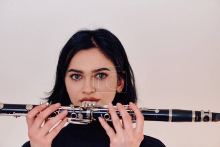 A talented brunette musician showcases her artistry as she gracefully holds and plays the clarinet against a pristine white background