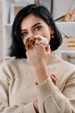 Foto de Una mujer de pelo negro disfruta de un día acogedor en casa con su ratón mascota, los dos compartiendo un momento lúdico en la cálida luz de la sala de estar. - Imagen libre de derechos
