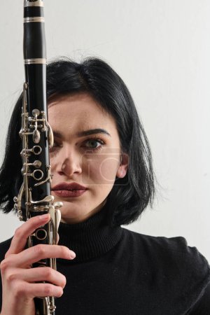 Eine talentierte brünette Musikerin zeigt ihre Kunstfertigkeit, als sie anmutig die Klarinette vor einem makellosen weißen Hintergrund hält und spielt