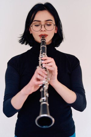 Téléchargez les photos : Une musicienne brune talentueuse met en valeur son art alors qu'elle tient gracieusement et joue de la clarinette sur un fond blanc immaculé - en image libre de droit