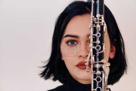 Photo for A talented brunette musician showcases her artistry as she gracefully holds and plays the clarinet against a pristine white background - Royalty Free Image