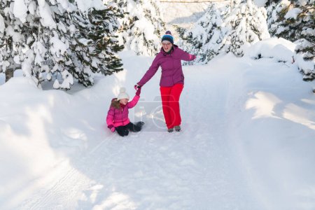 Eine Mutter und ihre Tochter flitzen auf einem ruhigen, verschneiten Pfad entlang und umarmen die ruhige Schönheit ihres Winterurlaubs in den Bergen.