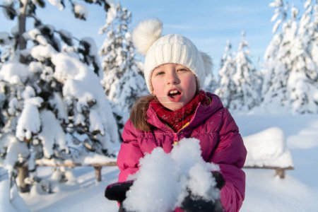 Join the enchanting journey of a delightful girl, adorned in her cozy winter attire, as she gleefully frolics and plays with the snow atop the sun-drenched mountain slopes.