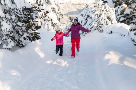 Eine Mutter und ihre Tochter flitzen auf einem ruhigen, verschneiten Pfad entlang und umarmen die ruhige Schönheit ihres Winterurlaubs in den Bergen.