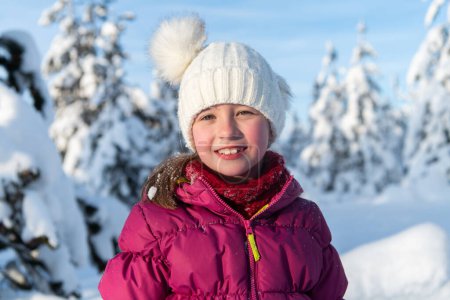 Foto de Una chica radiante sonríe con un telón de fondo de montañas cubiertas de nieve, el sol iluminando su expresión alegre. - Imagen libre de derechos