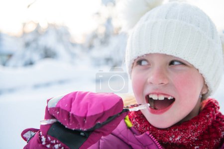 Téléchargez les photos : Mignonne petite fille tout en mangeant de la glace sur belle journée d'hiver. - en image libre de droit