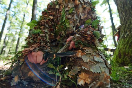 le sniper camouflé d'élite aiguise la concentration et les préparatifs pour la bataille dans la forêt dense, incarnant précision, furtivité et expertise alors qu'ils se préparent à une mission dans l'environnement forestier. 