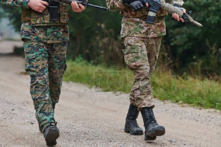 Foto aus nächster Nähe: Die widerstandsfähigen Beine von Elitesoldaten, bekleidet mit Tarnstiefeln, schreiten zielstrebig einen gefährlichen Waldweg entlang, als sie sich auf eine hochriskante militärische Mission begeben.. 