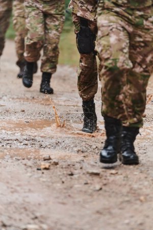 Foto de De cerca la foto, las piernas resistentes de los soldados de élite, vestidos con botas de camuflaje, caminan a propósito a lo largo de un peligroso sendero forestal mientras se embarcan en una misión militar de alto riesgo. - Imagen libre de derechos