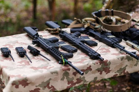 An array of military weapons, including rifles and pistols, is meticulously arranged on a table in a military base, presenting a close-up view of the diverse firepower and armament meticulously