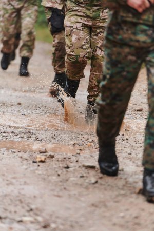 De cerca la foto, las piernas resistentes de los soldados de élite, vestidos con botas de camuflaje, caminan a propósito a lo largo de un peligroso sendero forestal mientras se embarcan en una misión militar de alto riesgo. 